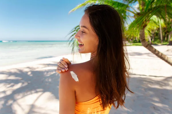 Güneş koruma kozmetik ürünleri. Bronzlaşmış omzuna güneş kremi süren bir kadın, Okyanus kıyısında duran, kopyalama alanı