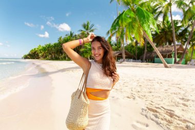 Kumsalda gülümseyen genç bir kadın, tropik bir adada tatilin tadını çıkarıyor, arka planda palmiyeler.