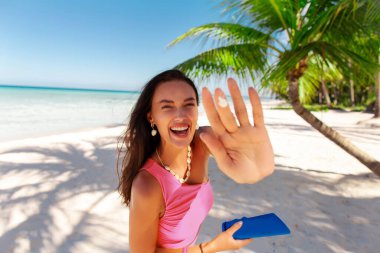 Neşeli kaygısız kadın elinde güneş kremi şişesiyle vücuduna krem ya da krem sürüyor güneşli bir yaz gününde okyanus sahilinde duruyor. Güneş koruma kavramı