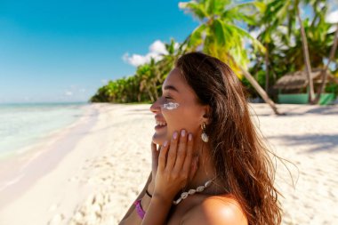 Tatmin olmuş bir kadının portresi güneş kremi sürüyor, güneş banyosu yapıyor ve okyanus kıyısında güneşleniyor.