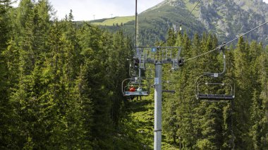 Yüksek köknar ağaçları ve sık orman manzarası olan yemyeşil dağın üzerinde kayak kaldıracı süzülüyordu.