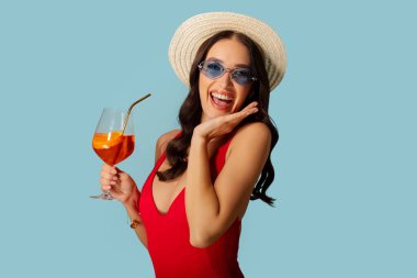 Mayo giymiş, elinde bardakla kokteyl tutan mutlu bir kadın. Lüks yaz tatilinin tadını çıkarıyor. Mavi arka planda yalnız poz veriyor.