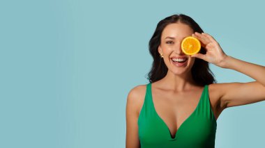 Yaz tazeliği konsepti. Mayo giymiş, gözleri turuncuyla kaplanmış, mavi stüdyo arka planında poz veren bir kadın.