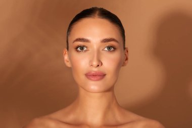 Kahverengi arka planda palmiye yaprağı gölgesi olan çekici Avrupalı bir kadının güzel portresi, sağlıklı ve berrak ciltli bir kadın. Kozmetik, cilt bakımı