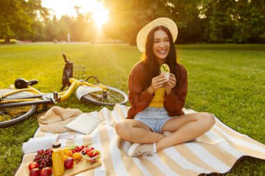 Piknik molası. Etli börek yiyen, sıcak yaz gününün tadını çıkaran, hafta sonu parkta takılan bir kadın.