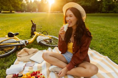 Rahat bir açık hava yemeği. Çimenlerin üzerinde piknik yaparken abur cubur yiyen bir kadın güneşli yaz gününde parkta dinleniyor.