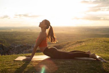 Yukarı doğru köpek pozisyonunda yoga yapan kadın, arka planda manzaralı dağlarda egzersiz yapıyor.