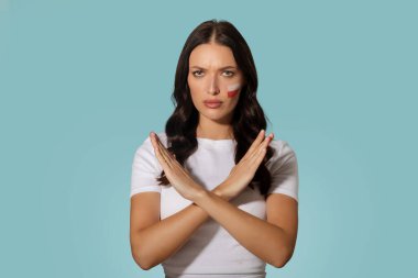 Kolları çapraz duran ve yanağında Polonya bayrağı olan ciddi bir kadın mavi arka planda poz veren kameraya bakıyor.