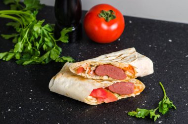 Tütsülenmiş sosis ve sebzeli sulu shawarma. Konsept: fast food. Domatesli, baharatlı ve otlu siyah arkaplan