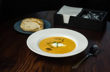 Koyu ahşap zemin üzerinde kavrulmuş balkabağı ve kremalı havuç çorbası ve kabak çekirdeği. Restoranda bir yemek.