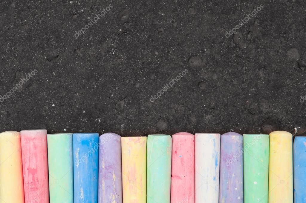 Colorful pastel sidewalk chalk on dark asphalt background. Stock Photo