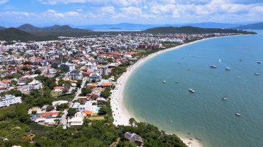 Florianpolis, Santa Catarina 'daki Jurer Uluslararası plajının panoramik hava manzarası, deniz kenarında lüks evler ve sahil kulüpleri, tekneler, yatlar ve turkuvaz mavisi okyanusta yelkenliler..