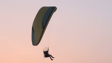 Motorlu bir paraglider akşam gökyüzünde uçuyor.
