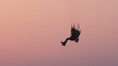 Motorlu bir paraglider akşam gökyüzünde uçuyor.