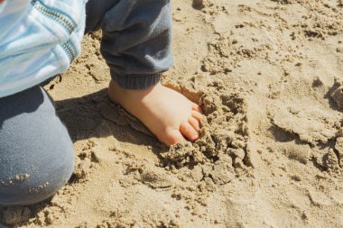 Ayağını plajda kumla dokunmadan erkek bebek