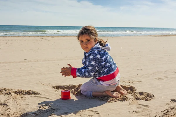 Ragazza che gioca con la sabbia in spiaggia in una giornata ventosa a Pasqua — Foto Stock