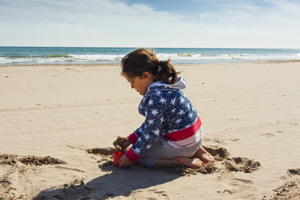 Ragazza che gioca con la sabbia in spiaggia in una giornata ventosa a Pasqua — Foto Stock