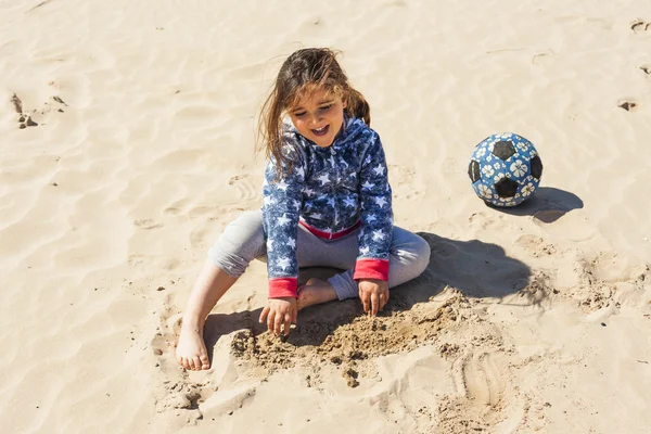 Ragazza sorridente che gioca con la sabbia in spiaggia in una giornata ventosa in — Foto Stock