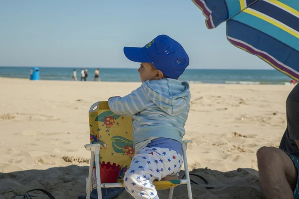 フルショットの男の子がビーチでプラスチック製のいすに立って. — ストック写真