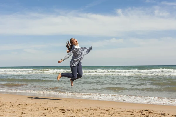 Full shot de un adolescente sonriente saltando en la orilla del mar de la bea — Foto de Stock