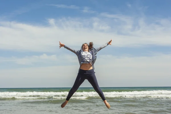 Full shot de un adolescente sonriente saltando en la orilla del mar de la bea — Foto de Stock