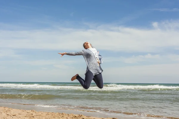 Full shot de un adolescente sonriente saltando en la orilla del mar de la bea — Foto de Stock