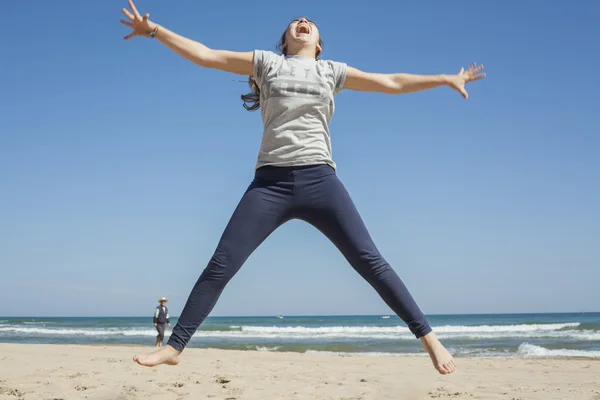Full shot de un adolescente sonriente saltando en la playa en un claro da — Foto de Stock