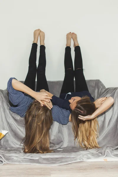 2 人の女の子を足でグレーのソファーに逆さまに敷設 — ストック写真