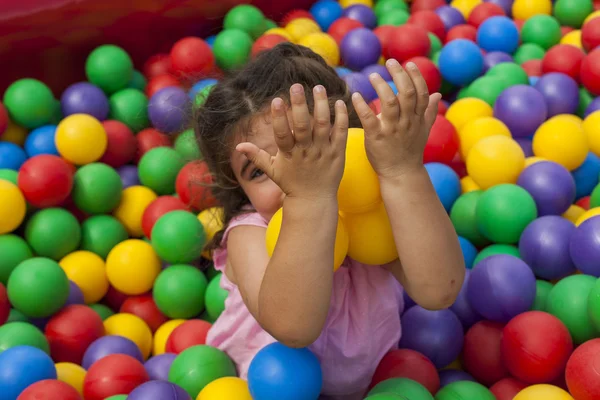 Menina se divertindo jogando com bolas amarelas em uma piscina de bolas — Fotografia de Stock