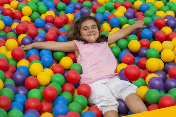 女孩躺在五颜六色的塑料球池 — 图库照片