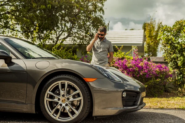 Plan moyen d'un jeune homme au téléphone, debout près d'une Porsche C — Photo