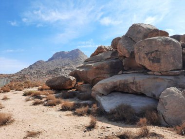 Tabuk 'taki Altın Kaya bölgesinin çarpıcı gündüz perspektifi. Tarihi kırmızı kayalar, parlayan çöl kumları ve berrak mavi gökyüzü birleşerek pitoresk bir manzara oluşturuyor..