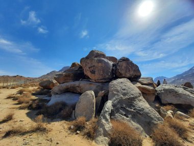 Tabuk 'taki Altın Kaya bölgesinin çarpıcı gündüz perspektifi. Tarihi kırmızı kayalar, parlayan çöl kumları ve berrak mavi gökyüzü birleşerek pitoresk bir manzara oluşturuyor..