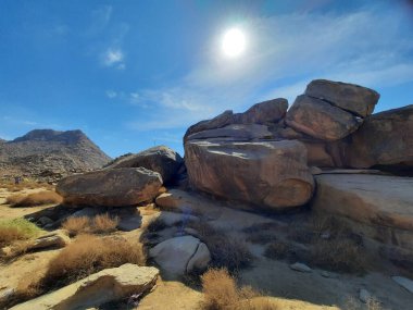 Tabuk 'taki Altın Kaya bölgesinin çarpıcı gündüz perspektifi. Tarihi kırmızı kayalar, parlayan çöl kumları ve berrak mavi gökyüzü birleşerek pitoresk bir manzara oluşturuyor..
