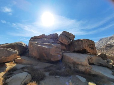 Tabuk 'taki Altın Kaya bölgesinin çarpıcı gündüz perspektifi. Tarihi kırmızı kayalar, parlayan çöl kumları ve berrak mavi gökyüzü birleşerek pitoresk bir manzara oluşturuyor..