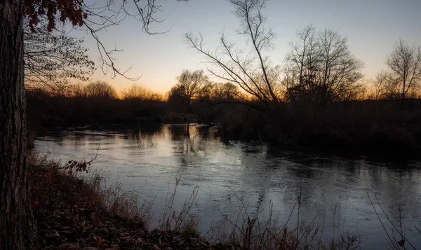 Sakin bir nehir, alacakaranlıkta sessiz bir ormanlık arazide yavaşça akar, batan güneşin sıcak, huzurlu parıltısıyla yıkanır, sakin ve doğal güzelliği anımsatır..