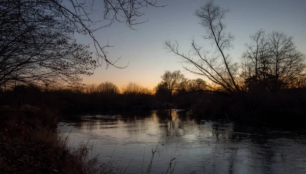 Sakin bir akşam sahnesi, sakin suya yansıyan alacakaranlığın yumuşak parıltısını yakalar, ağaçların ve sazlıkların karanlık siluetleriyle çevrili, derin bir huzur hissi uyandırır..