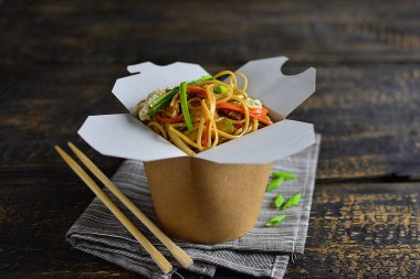 Geleneksel Çin eriştesi sebzeli ve etli, çubuklu bir kutuda, siyah ahşap arka planda, kopyalama alanı.