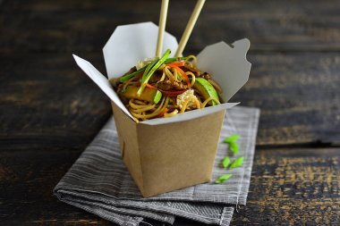 Geleneksel Çin eriştesi sebzeli ve etli, çubuklu bir kutuda, siyah ahşap arka planda, kopyalama alanı.