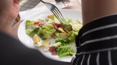 Restoranda Sezar Salatası yiyen bir kadın. Kıtır marul, yumurta, tütsülenmiş biftek, çıtır çıtır ekmek, parmesan peyniri ve hafif Sezar sosuyla servis edilir.