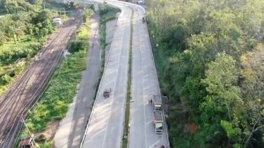 Uzun asfalt bir yoldan geçen araçların hava görüntüsü, hala sık ormanlarla çevrili.
