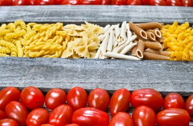 Ahşap tabakta makarna ve küçük kırmızı domates çeşitli karışımı