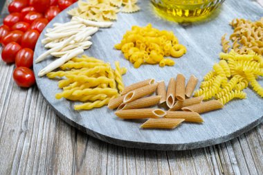 Various mix of pasta, small red tomatoes and olive oil on wooden