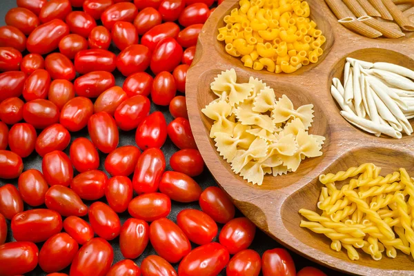 Ahşap kase makarna çeşitli karışımı, küçük kırmızı domates closeup