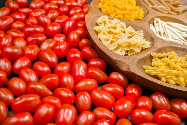 Ahşap kase makarna çeşitli karışımı, küçük kırmızı domates closeup
