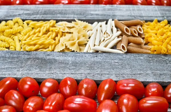 Ahşap tabakta makarna ve küçük kırmızı domates çeşitli karışımı