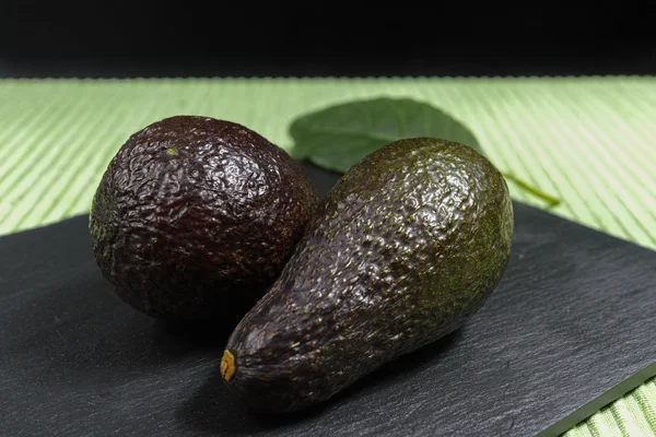 Frische reife Bio-Avocado auf grünem und schwarzem Hintergrund — Stockfoto
