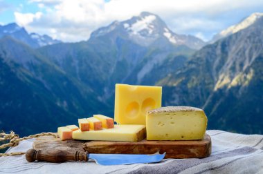 Peynir koleksiyonu, Fransız beaufort, abondance, emmental, tomme de savoie cheeses Savoy bölgesinde açık havada servis edilir, yaz aylarında Alp dağlarının zirveleri arka plandadır.