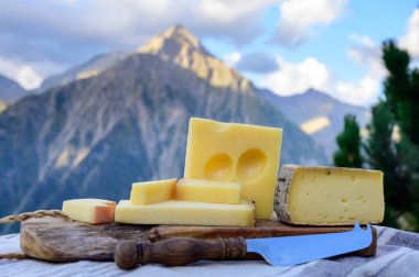 Peynir koleksiyonu, Fransız beaufort, abondance, emmental, tomme de savoie cheeses Savoy bölgesinde açık havada servis edilir, yaz aylarında Alp dağlarının zirveleri arka plandadır.
