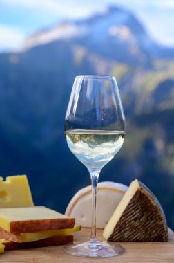 Fransa 'nın Savoy bölgesinden lezzetli peynir ve şarap, Beaufort, abondance, emmental, tomme ve reblochon de savoie peynirleri ve yazın açık havada sunulan beyaz şarap arka planda Alp dağlarının zirveleri